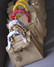 Afbeelding in Gallery-weergave laden, Burlap O'Kelly handbag tote bags with colorful scarf-wrapped handles lined up on a gray surface