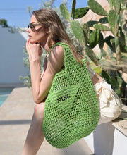 Cargar imagen en el visor de la galería, Handmade raffia bucket bag in green worn by woman sitting outdoors near cactus plants