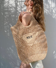 Cargar imagen en el visor de la galería, Handmade raffia bucket bag tote by Travellers Hat Boutique worn by woman in natural light
