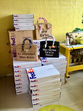 Load image into Gallery viewer, 35cm printed burlap bag collection from Travellers Hat Boutique displayed near stacked FedEx boxes

