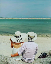 Load image into Gallery viewer, Bride and groom wearing custom prenuptial hat set with names on a beach by the ocean
