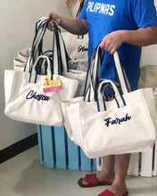 Lataa kuva Galleria-katseluun, Travellers Hat Boutique embroidered boat tote bag in white with navy striped handles and personalized names Chesca and Farah
