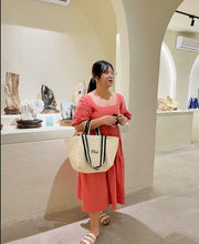 Lataa kuva Galleria-katseluun, Woman wearing a coral dress holding an embroidered boat tote bag with black handles from Travellers Hat Boutique
