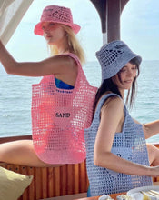 Carregar imagem no visualizador da galeria, Two women wearing handmade raffia bucket bags in pink and blue while sitting on a boat by the sea
