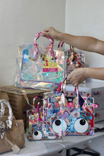 Carregar imagem no visualizador da galeria, Traveller Hat Boutique holographic clear tote bag with pink handles and colorful cartoon designs
