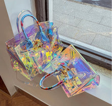 Carregar imagem no visualizador da galeria, Travellers Hat Boutique holographic clear tote bag with colorful handles displayed on windowsill
