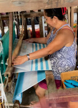 Load image into Gallery viewer, Woman weaving a personalized beach towel with blue and white stripes on a traditional loom
