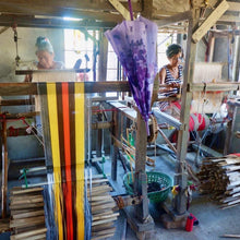 Load image into Gallery viewer, Two women weaving colorful fabric on traditional wooden looms in a workshop for personalized beach towel accessories
