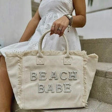 Lade das Bild in den Galerie-Viewer, Personalized canvas tote with fringe and beaded Beach Babe text held by woman in white dress

