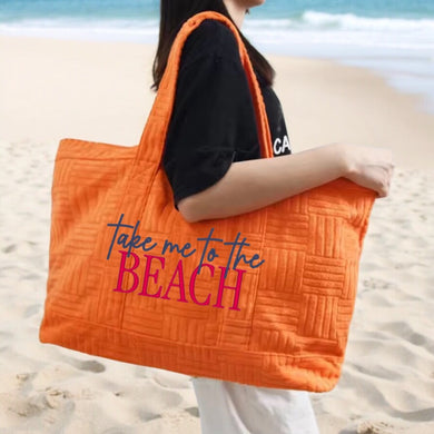 Orange terry cloth beach tote bag with take me to the beach print carried by woman on sandy shore