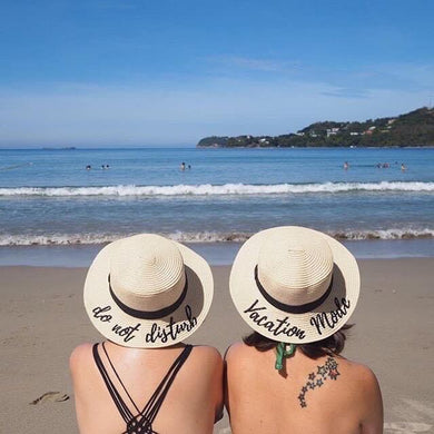 Two women wearing custom embroidered round hats with beach and ocean background at a sunny beach