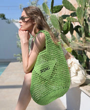 Carregar imagem no visualizador da galeria, Handmade raffia bucket bag in green worn by woman sitting outdoors near cactus plants
