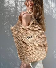 Carregar imagem no visualizador da galeria, Handmade raffia bucket bag tote by Travellers Hat Boutique worn by woman in natural light
