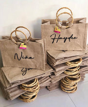 Load image into Gallery viewer, Stack of personalized jute tote bag with bamboo handle featuring custom names in black script
