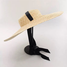 Lade das Bild in den Galerie-Viewer, Large wheat straw hat with wide brim and black ribbon band on display stand
