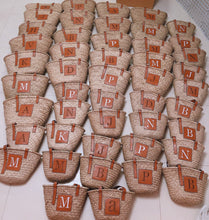 Lade das Bild in den Galerie-Viewer, Multiple seagrass basket handbags with leather straps and initial patches arranged in rows from Travellers Hat Boutique
