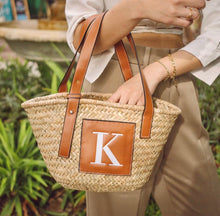 Lade das Bild in den Galerie-Viewer, Traveller Hat Boutique seagrass basket handbag with leather straps and monogram patch being carried
