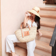 Lade das Bild in den Galerie-Viewer, Seagrass basket handbag with leather straps and monogram detail carried by woman in white outfit sitting on stairs
