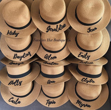 Carregar imagem no visualizador da galeria, Custom embroidered round hat collection from Travellers Hat Boutique featuring names on tan straw hats with black bands
