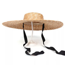 Lade das Bild in den Galerie-Viewer, Wheat straw hat with ribbon in black featuring wide brim and adjustable ties on display stand

